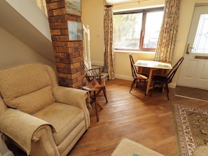 A living room with a brick fireplace, a sofa, a dining table with chairs, and a window with curtains.