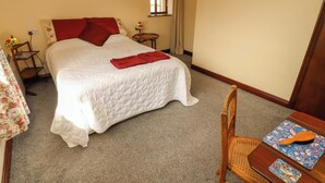 A neatly made bed with a red blanket, a small wooden table with a brush and a patterned tray, and a window with curtains. - Burn Bank (Appleby-in-Westmorland)