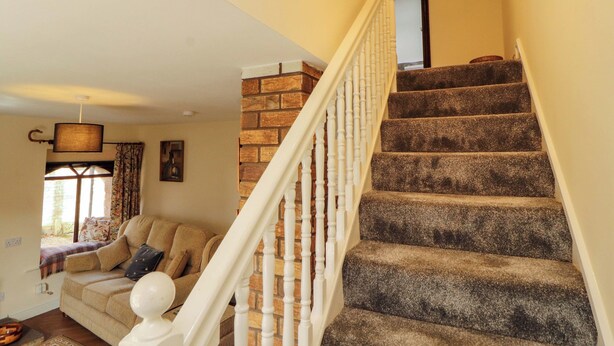 A staircase with a brick wall and white balusters, leading to a room with a beige sofa and a window with curtains. - Burn Bank (Appleby-in-Westmorland)