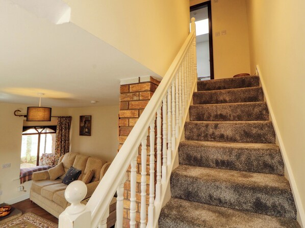 A staircase with a brick wall and white balusters, leading to a room with a beige sofa and a window with curtains.