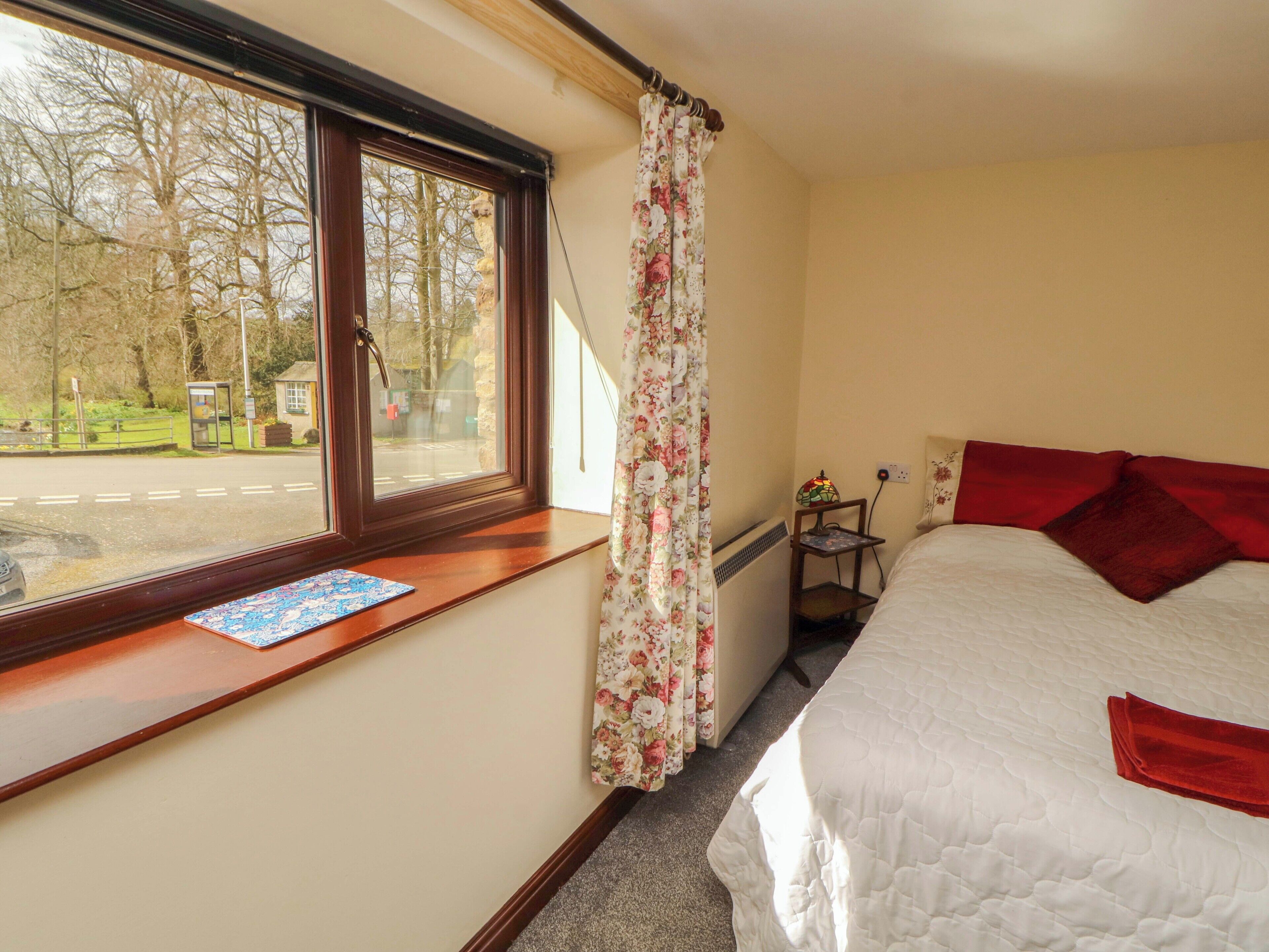 A bedroom with a bed, a window with curtains, a bedside table, and a lamp.