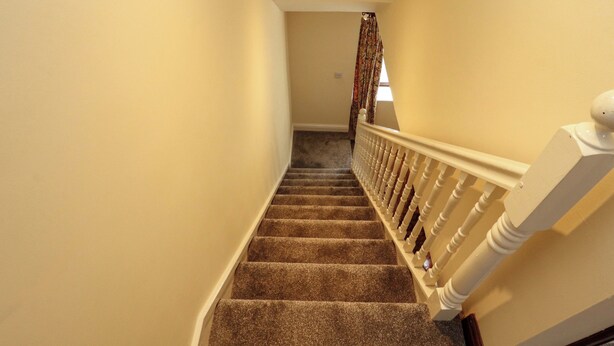 A carpeted staircase with white balusters, a plain wall, and a window with a curtain. - Burn Bank (Appleby-in-Westmorland)