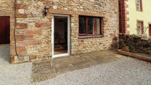 A stone building with a door leading to an interior room, a window, and a small garden area. - Burn Bank (Appleby-in-Westmorland)