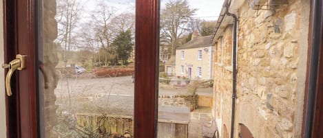 A window with a view of a stone building, a paved area, and bare trees.
