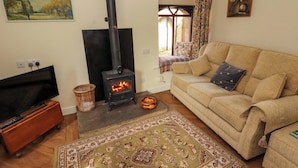 A living room with a sofa, a television, a fireplace, a painting, and a window with curtains. - Burn Bank (Appleby-in-Westmorland)