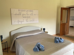 Un dormitorio con una cama grande, una mesita de noche con lámpara, una pared con una cita motivacional y una puerta que da a otra habitación.