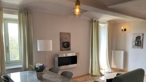 Ein modernes Wohnzimmer mit Esstisch, Stühlen, einer Couch, einem an der Wand befestigten Fernseher und einem Fenster mit Vorhängen.