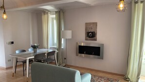 Ein Wohnzimmer mit Sofa, einem Esstisch mit Stühlen, einem flachbildfernseher an der Wand und einem gemusterten Teppich.