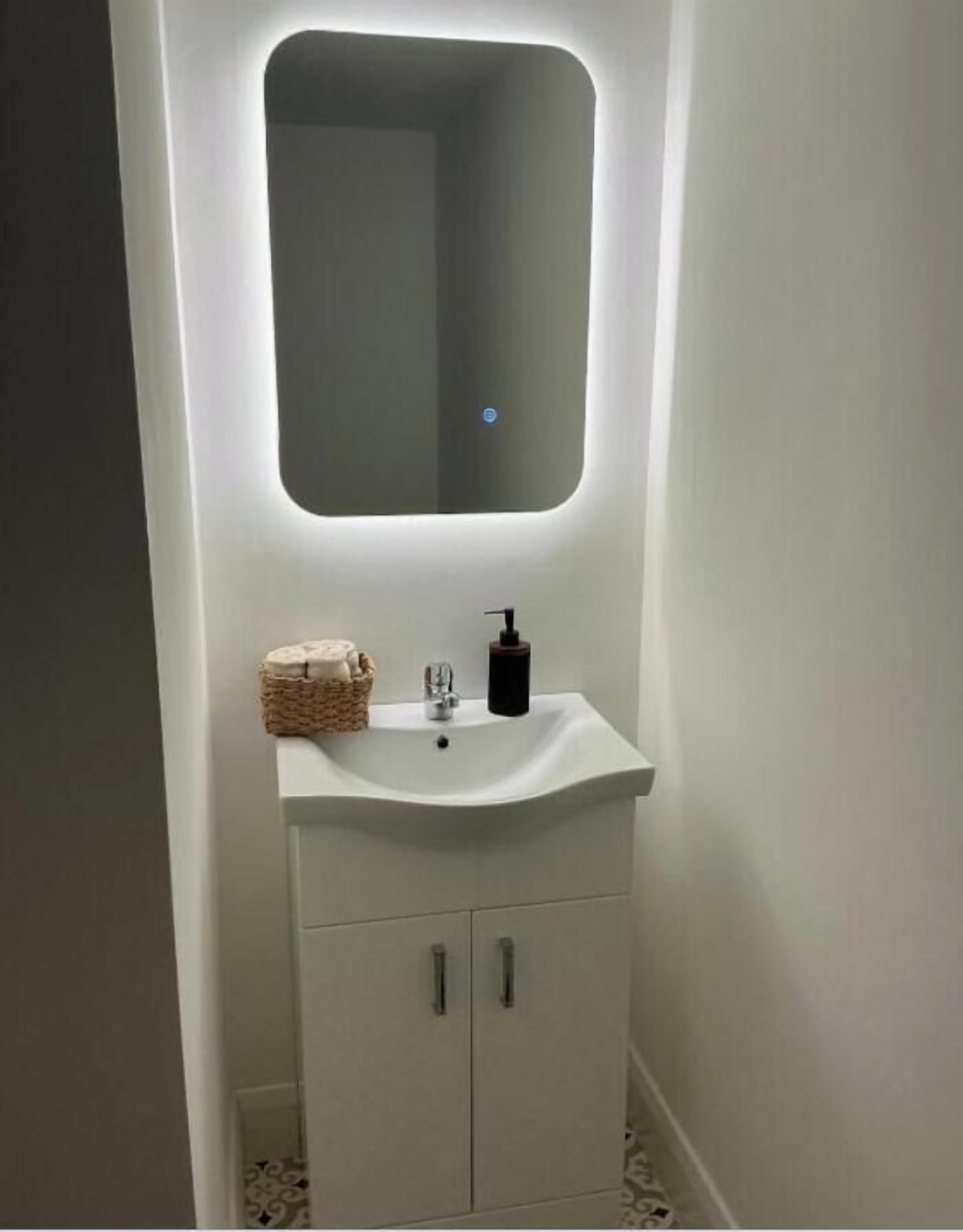 A bathroom with a white sink, a mirror, and a small basket of toiletries.