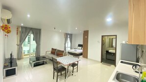Ein modernes Wohnzimmer mit Sofa, Esstisch und Stühlen, einer Küchenzeile mit Spüle und einem großen Fenster mit Vorhängen.