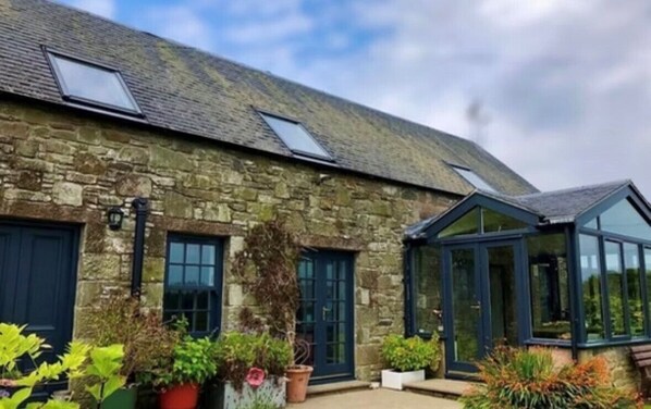 A stone building with two windows, a conservatory, and potted plants. - Trossachs Barn & Cabin (Stirling)