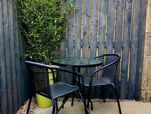 A small outdoor patio with a round table and two chairs, surrounded by a wooden fence and a potted plant. - Trossachs Barn & Cabin (Stirling)