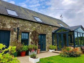 A stone house with a conservatory, potted plants, and a clear sky. - Trossachs Barn & Cabin (Stirling)