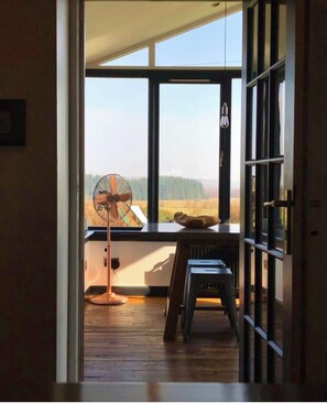 A room with a large window, a fan, and a small stool. - Trossachs Barn & Cabin (Stirling)