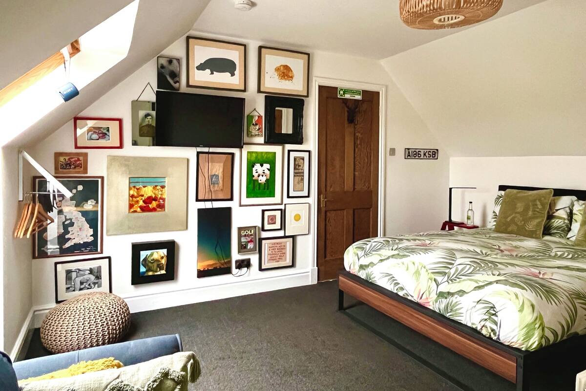 A bedroom with a sloped ceiling, a bed with a floral bedspread, a wall-mounted TV, and various framed pictures.