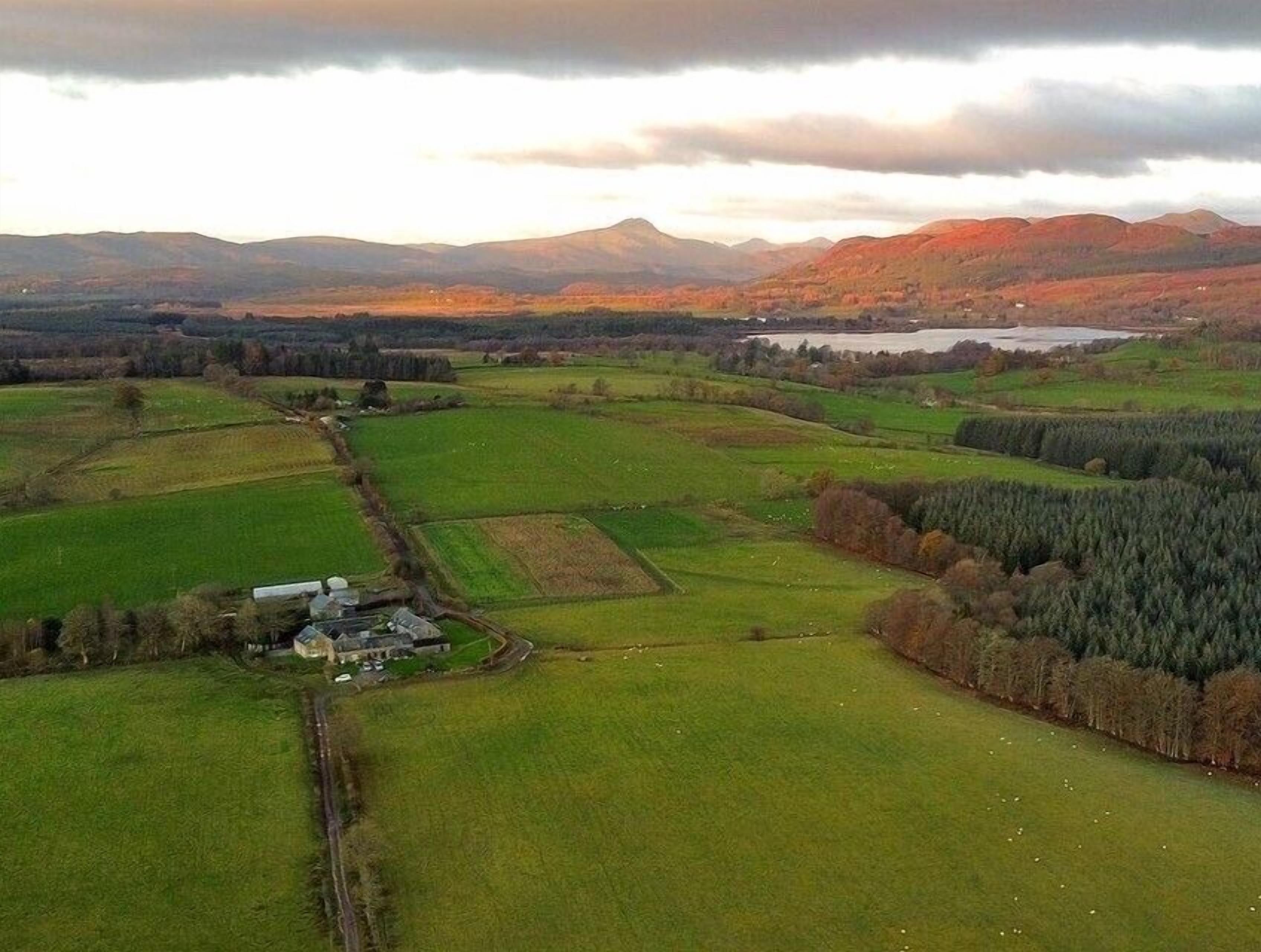 A rural landscape with fields, a small building, and distant mountains.