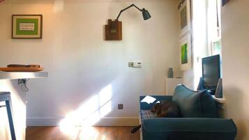 Een woonkamer met een blauwe bank, een hond, een bureau met een computer en een wandlamp.