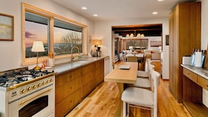 A modern kitchen with wooden cabinets, a gas stove, and a dining area with a wooden table and chairs.