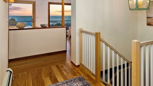 A wooden-floored hallway leading to a balcony with a view of the sunset.