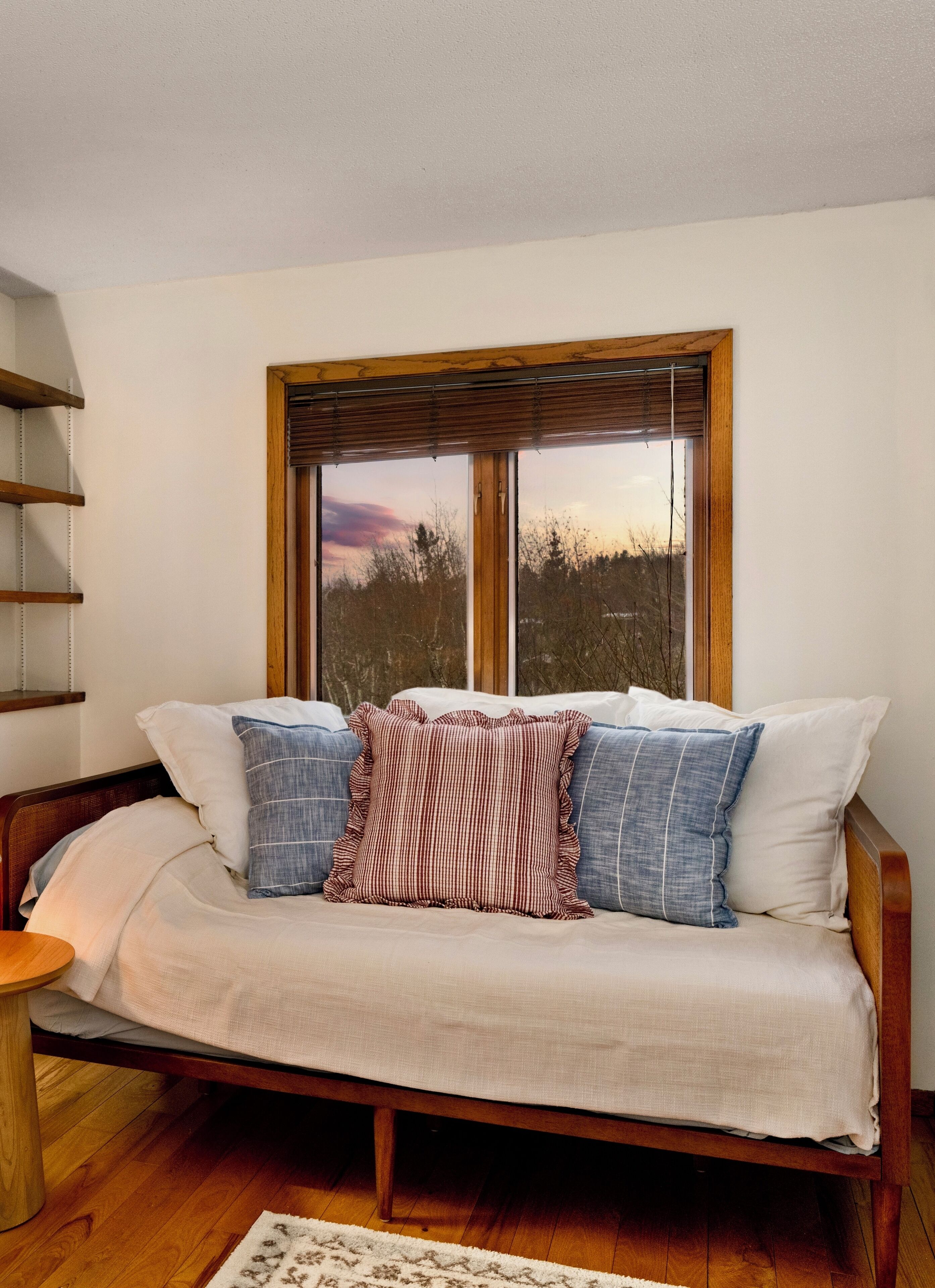 A room with a wooden-framed window, a sofa with patterned cushions, and a wooden floor.