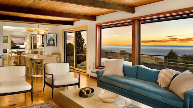 A spacious living area with a large window offering a view of the ocean, a blue sofa, and a dining area with natural light.