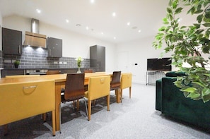 A modern kitchen with a dining area, a flat-screen TV, and a green plant. - Suite of 3 Delux 2-bedroom apartments. Parties are welcome (Thatcham)