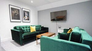 Un salon avec un canapé vert, une table basse en bois et un téléviseur à écran plat fixé au mur.