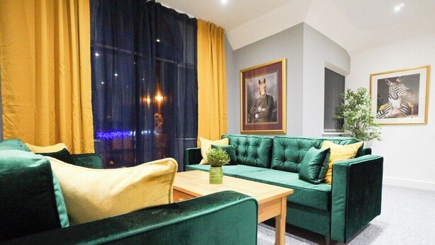 Une pièce avec un canapé vert, une table basse en bois et une plante. Deux tableaux encadrés sont accrochés au mur.