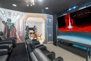 Un salón de cine en casa con un cartel de Star Wars, un televisor de pantalla plana grande y una zona de estar con sillones de cuero negro.