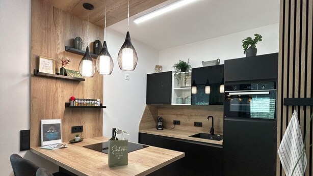 Une cuisine moderne avec un îlot central en bois, des luminaires suspendus et un plan de travail noir.