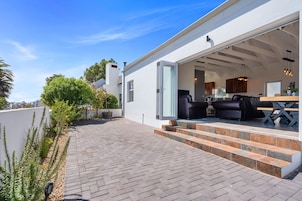 Una casa moderna con patio, mobiliario exterior y un área de cocina visible.