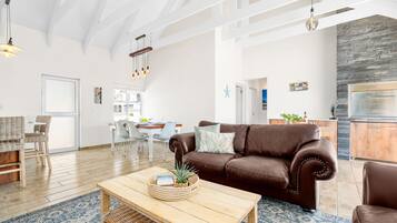 A spacious living room with a brown leather sofa, a wooden coffee table, and a dining area with white chairs.