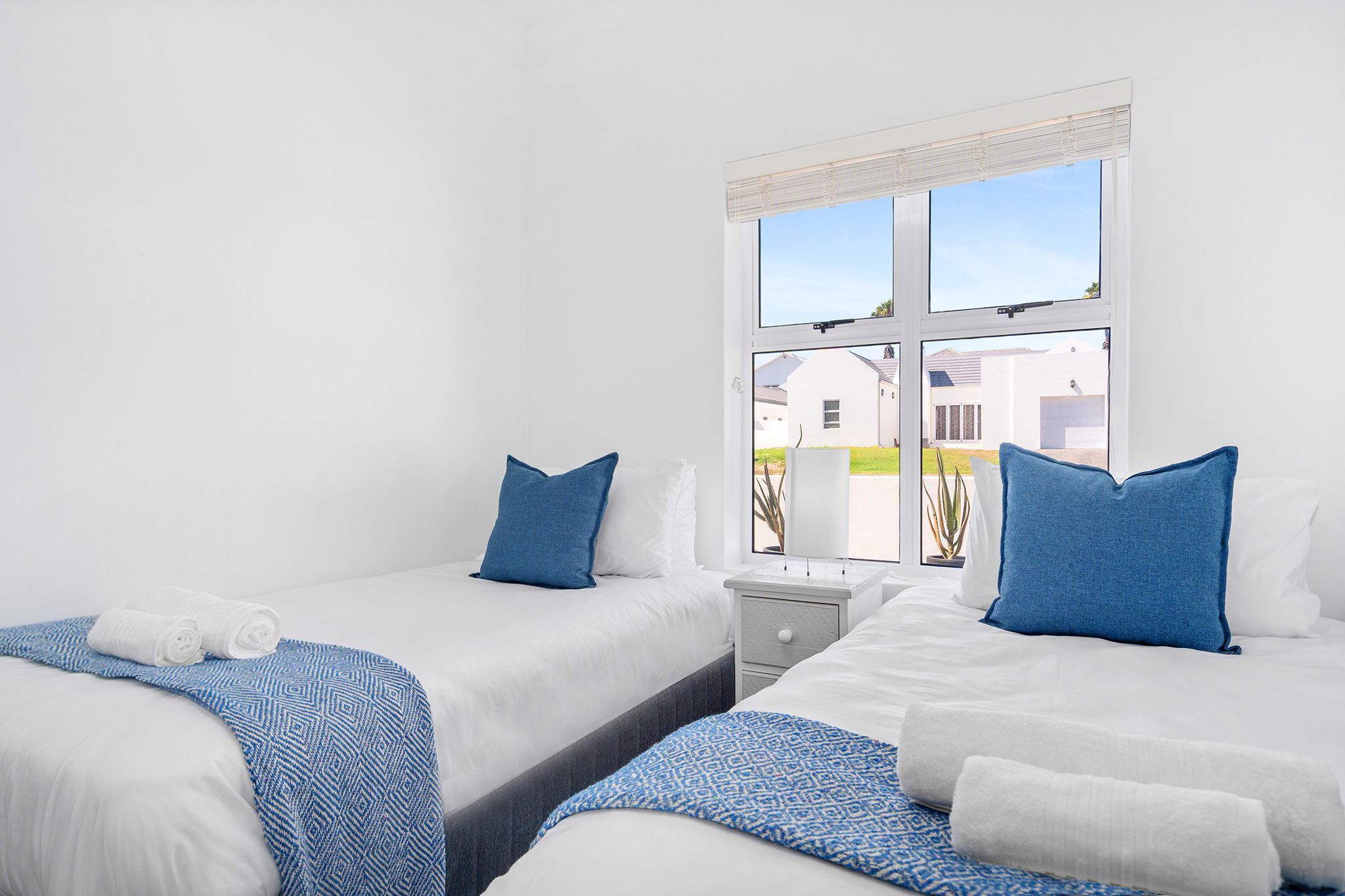 Une chambre d’hôtel avec deux lits, une table de chevet et une fenêtre donnant sur des immeubles.