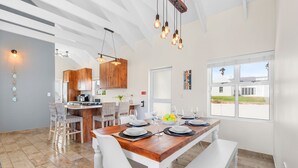 A modern kitchen with wooden cabinets, a dining area with a wooden table and white chairs, and a large window offering a view of the outside. - Shelley Point 36 on 20th Street (St. Helena Bay)
