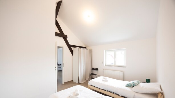 A bedroom with two single beds, a window, a radiator, and a door leading to another room.