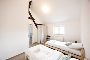 A bedroom with two single beds, a window, a radiator, and a door leading to another room.