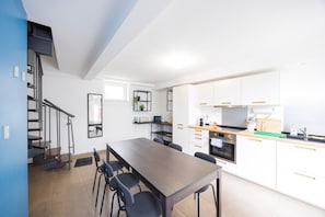 Une cuisine moderne avec des meubles blancs, une table à manger en bois et un escalier doté de rampes en métal.