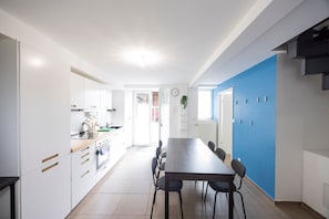 Une cuisine moderne avec des meubles blancs, un plan de travail en bois et un coin repas comprenant une longue table et des chaises.
