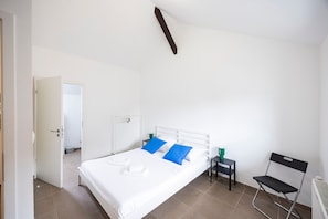 Une chambre à coucher avec un lit, des oreillers, une chaise, une table et un radiateur.