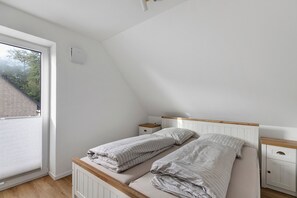 Ett sovrum med ett sluttande tak, ett fönster, en säng med två kuddar, ett sängbord och ett litet bord.