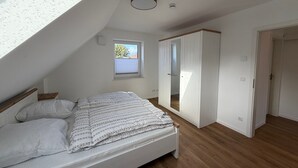 Een slaapkamer met dakraam, een bed, een garderobe en een klein raam.