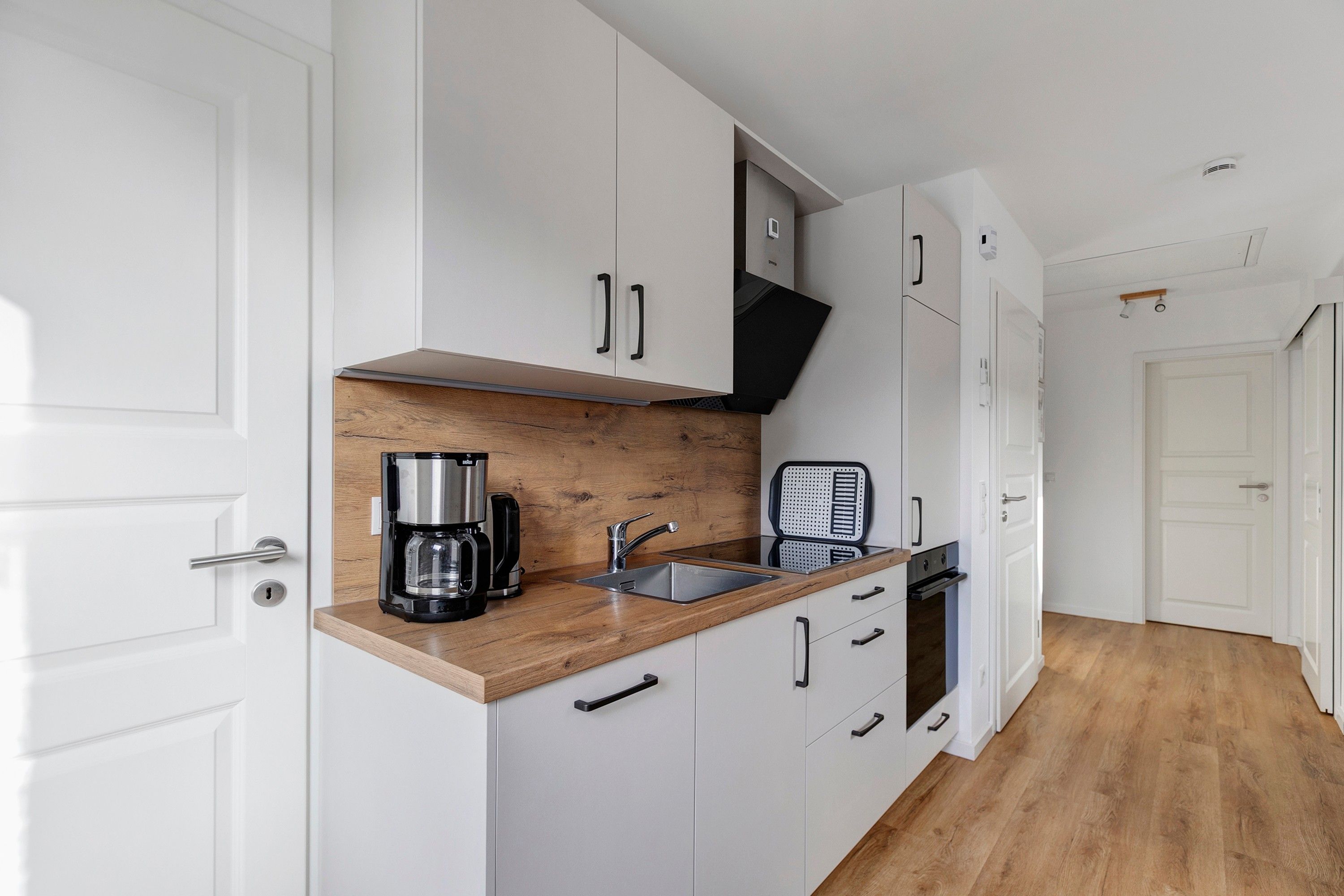 A compact kitchen with white cabinets, a wooden countertop, a coffee maker, a kettle, and a toaster.