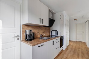 Ett kompakt kök med vita skåp, en träbänkskiva, en kaffebryggare, en vattenkokare och en brödrost.