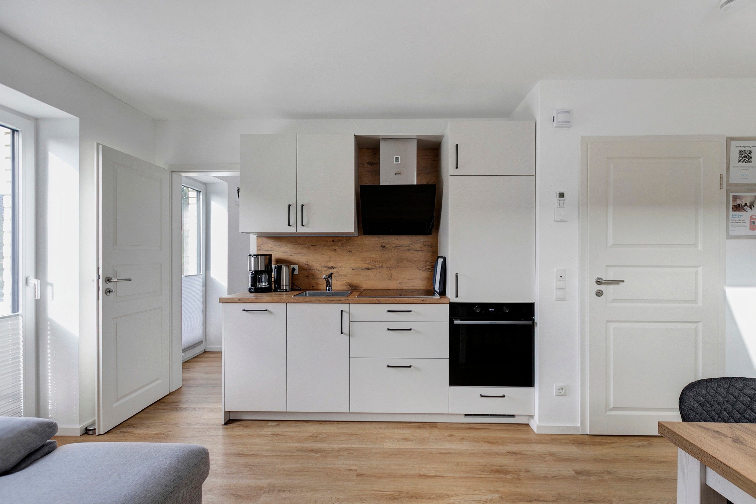 Eine kleine Küche mit weißen Schränken, einer Holz Arbeitsplatte, einer Kaffeemaschine und einem schwarzen Backofen.