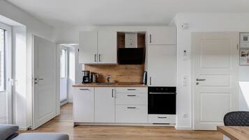Een kleine keuken met witte kastjes, een houten aanrecht, een koffiezetapparaat en een zwarte oven.
