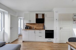 Una cocina compacta con armarios blancos, una encimera de madera, cafetera y horno negro.
