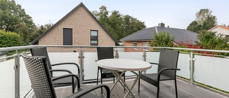 A balcony with a table and two chairs, a metal railing, and a building in the background.