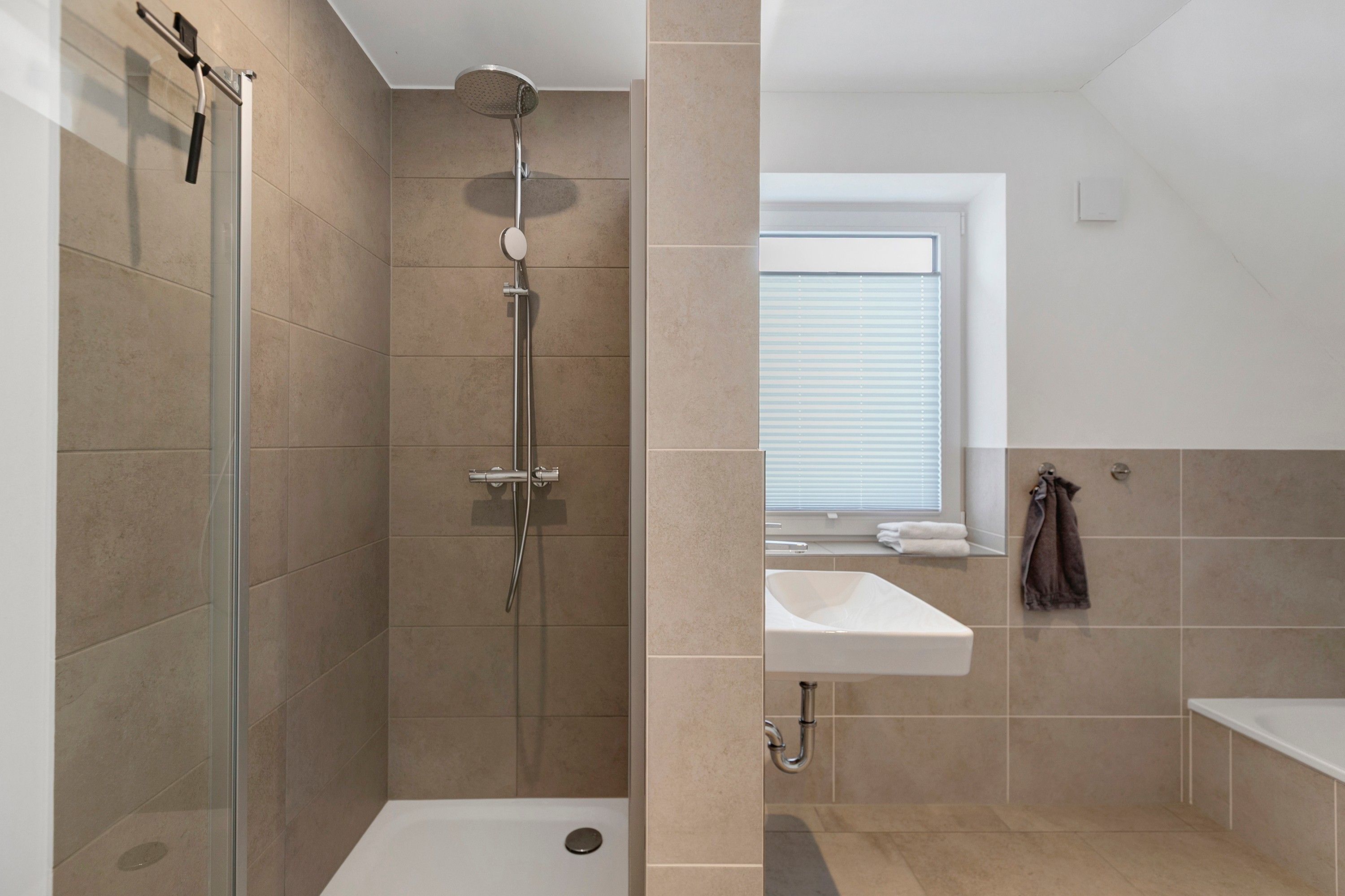 A modern bathroom with a glass-enclosed shower, a white sink, and a window providing natural light.