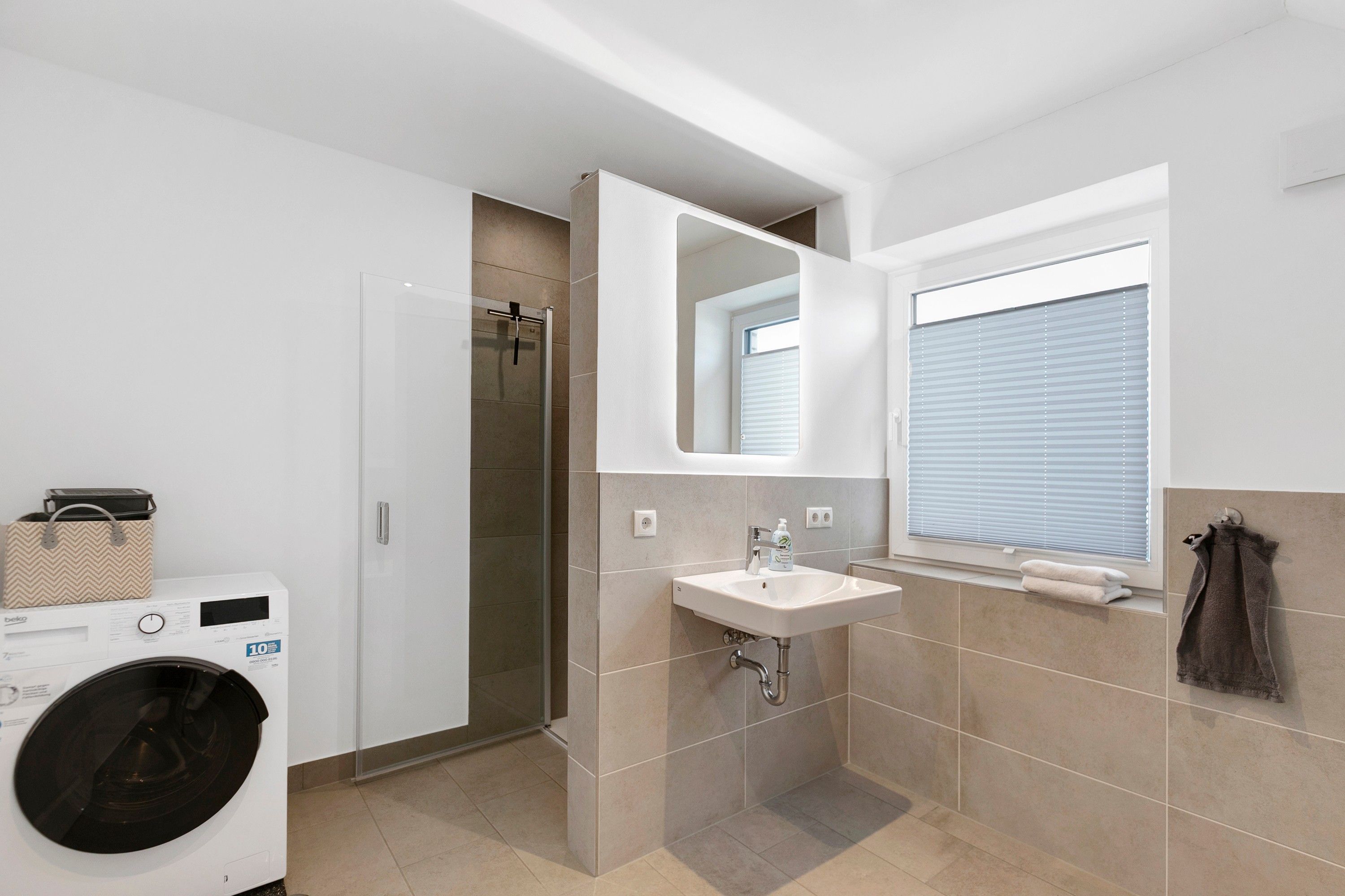 Ein modernes Badezimmer mit integrierter Waschmaschine, Waschbecken und Dusche.