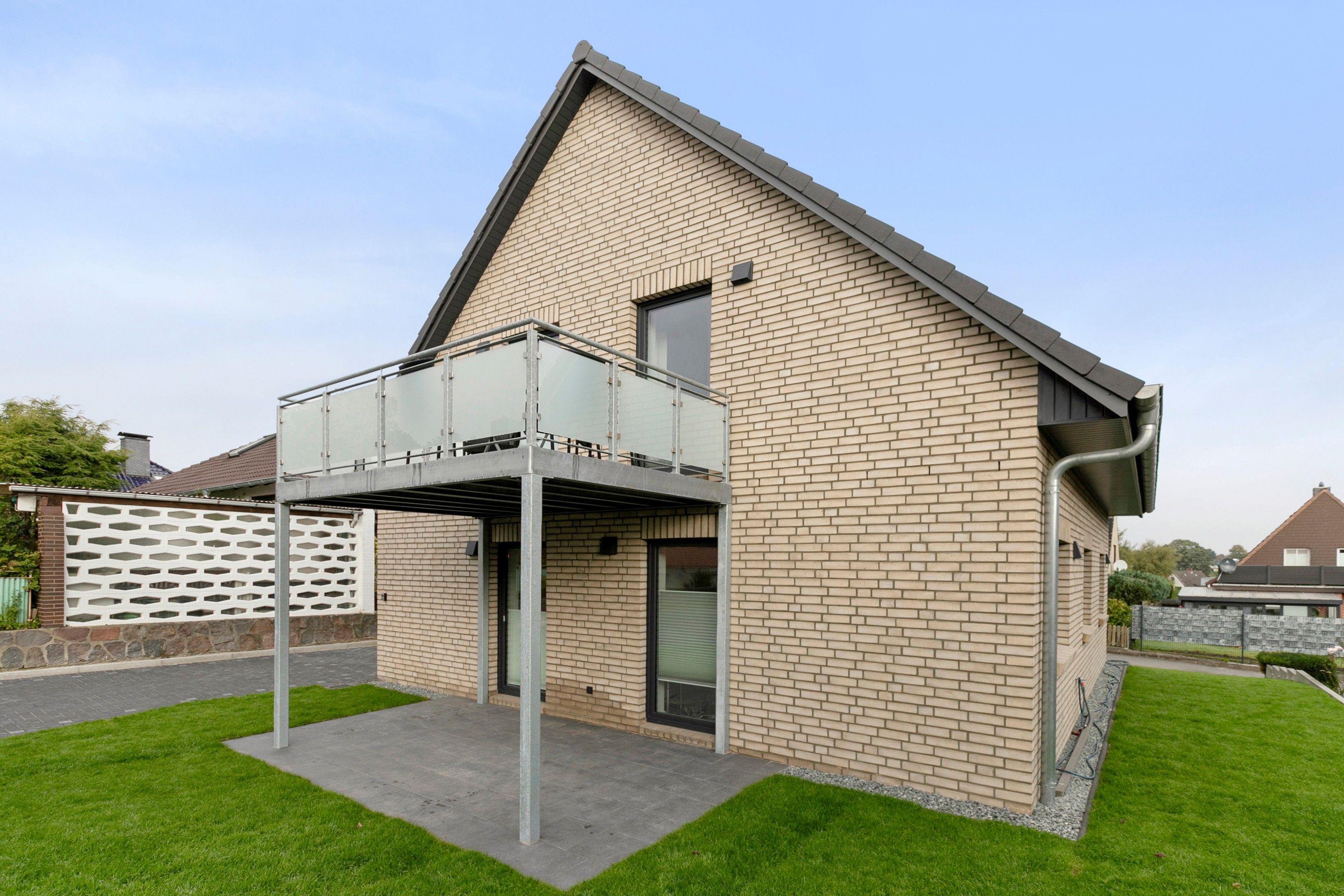 Een modern huis met een bakstenen gevel, een balkon en een verzorgd gazon.